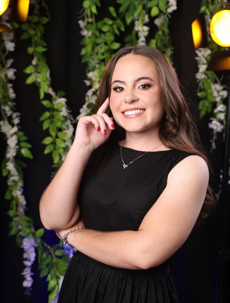 Foto de Tamiris sorrindo de vestido preto e fundo com folhagens